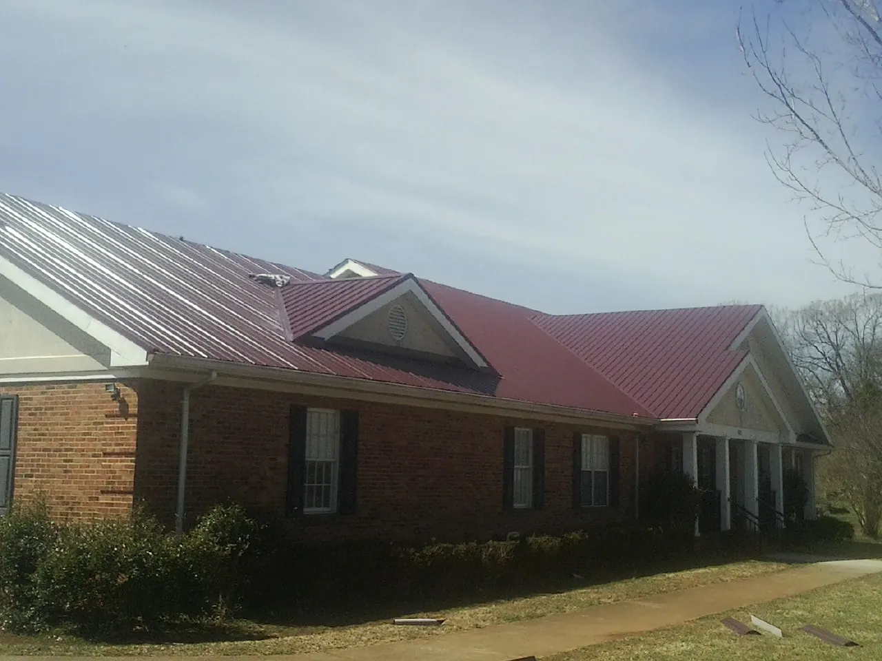 Red metal roof with gabled entries on a long brick building, from a Hail Damage Roof Repair job in South Holland