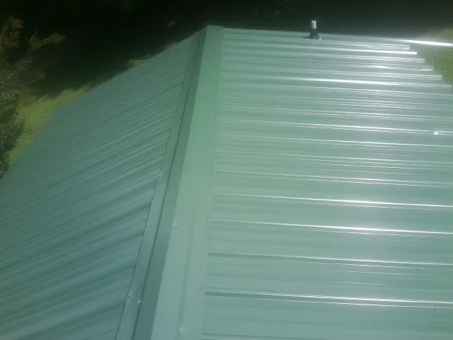 New green metal panels meeting at the ridge of a roof — Flat Roof Repair work by our crew in South Holland
