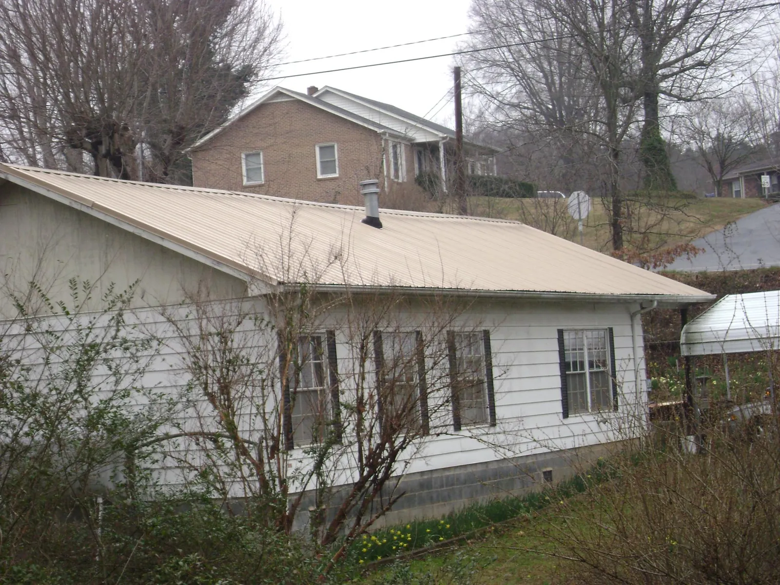 Tan metal roof on a white sided house set into a hillside — Commercial Roofing by Roofing Brothers in South Holland
